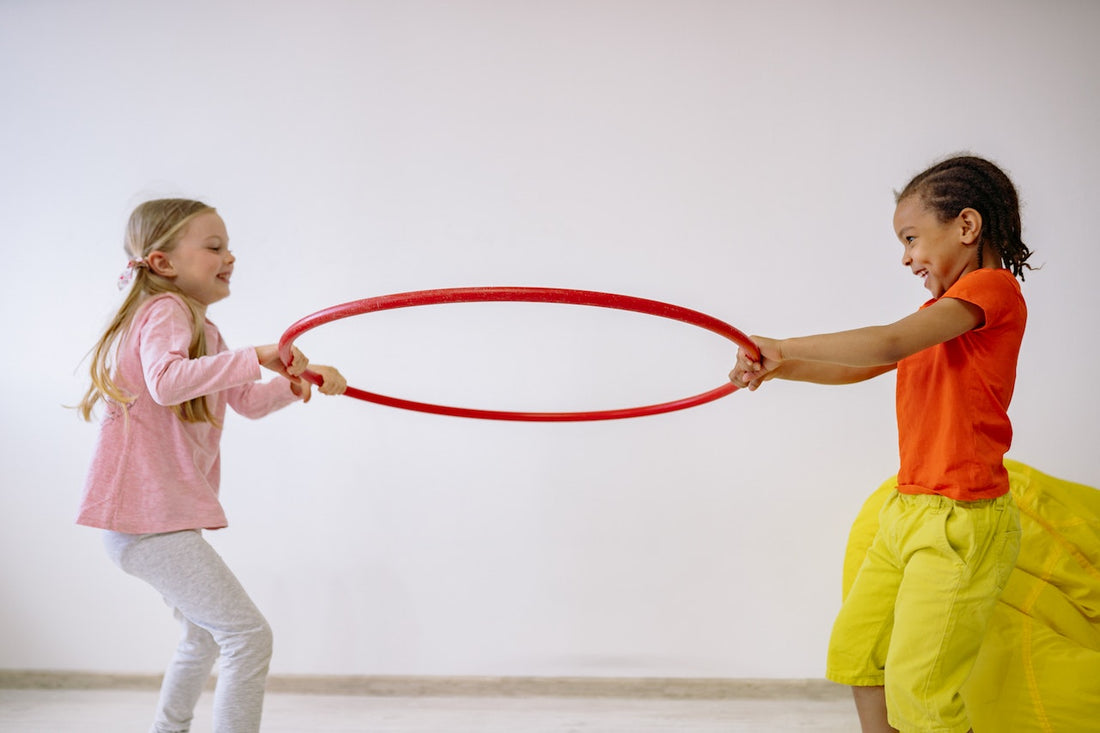 Two small children holding on to an orange colored hula hoop.